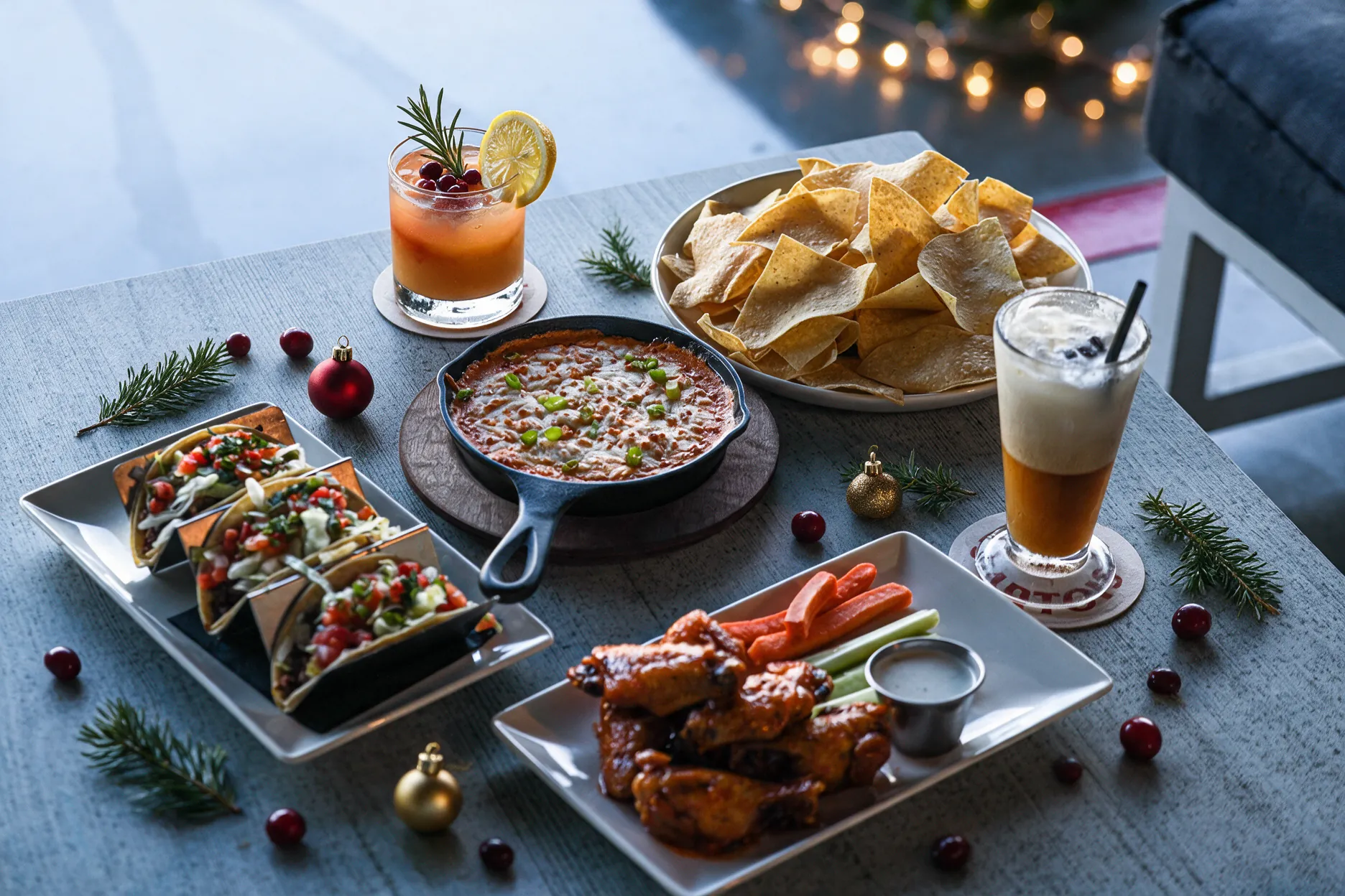 Tacos, queso skillet, chips, wings, and cocktails styled with holiday greenery and ornaments.